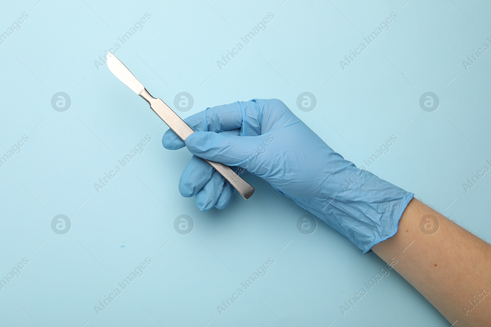 Photo of Doctor with surgical scalpel on light blue background, top view