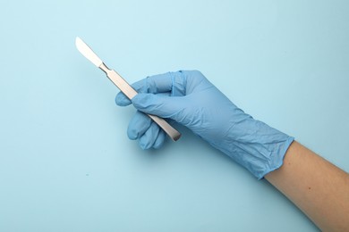 Photo of Doctor with surgical scalpel on light blue background, top view