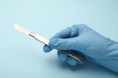 Photo of Doctor with surgical scalpel on light blue background, closeup