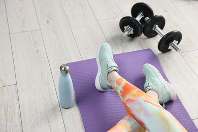 Photo of Woman with barbells and thermo bottle on floor indoors, closeup