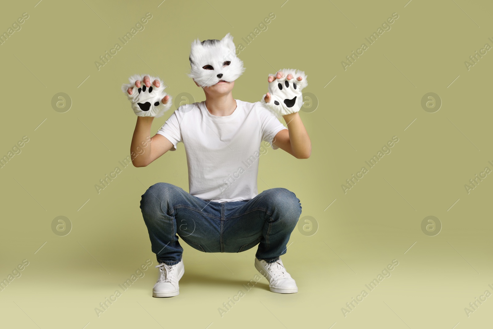 Photo of Quadrobics. Boy wearing cat mask and gloves on pale olive background