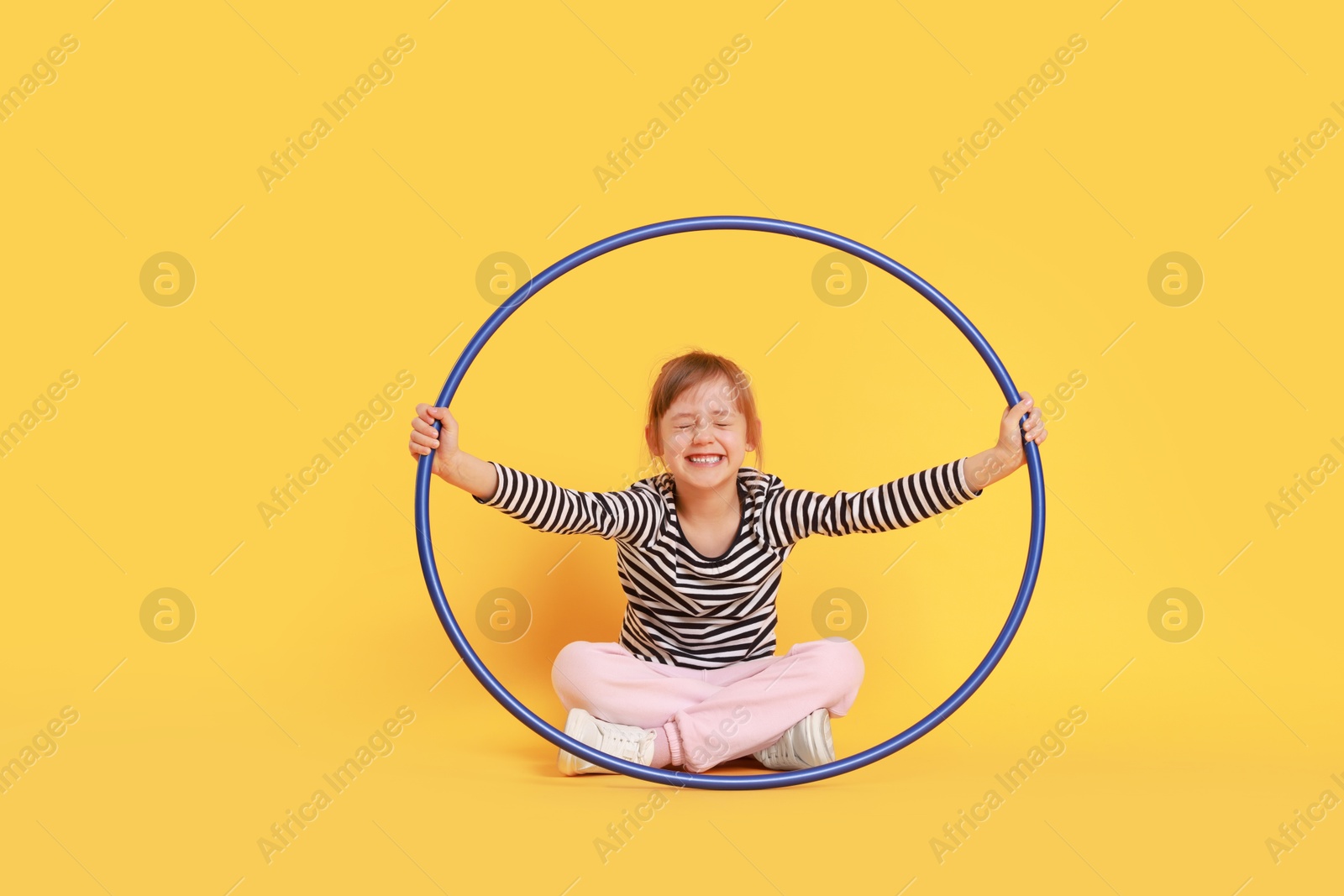 Photo of Cute little girl with hula hoop on orange background