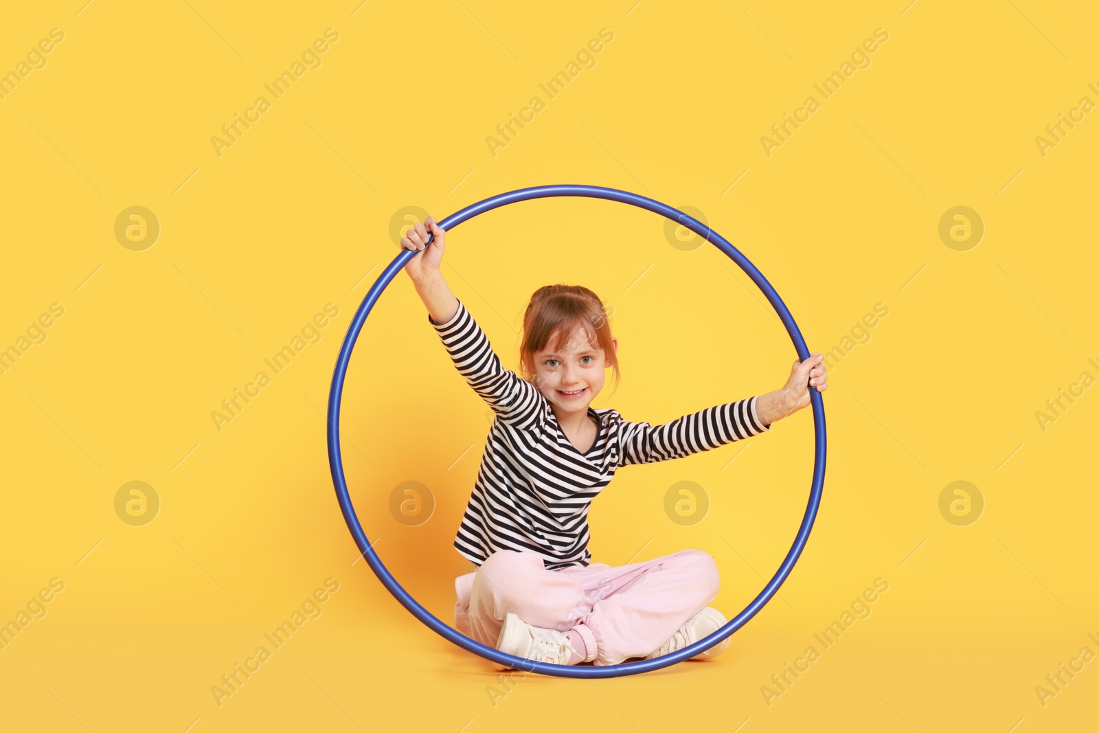 Photo of Cute little girl with hula hoop on orange background