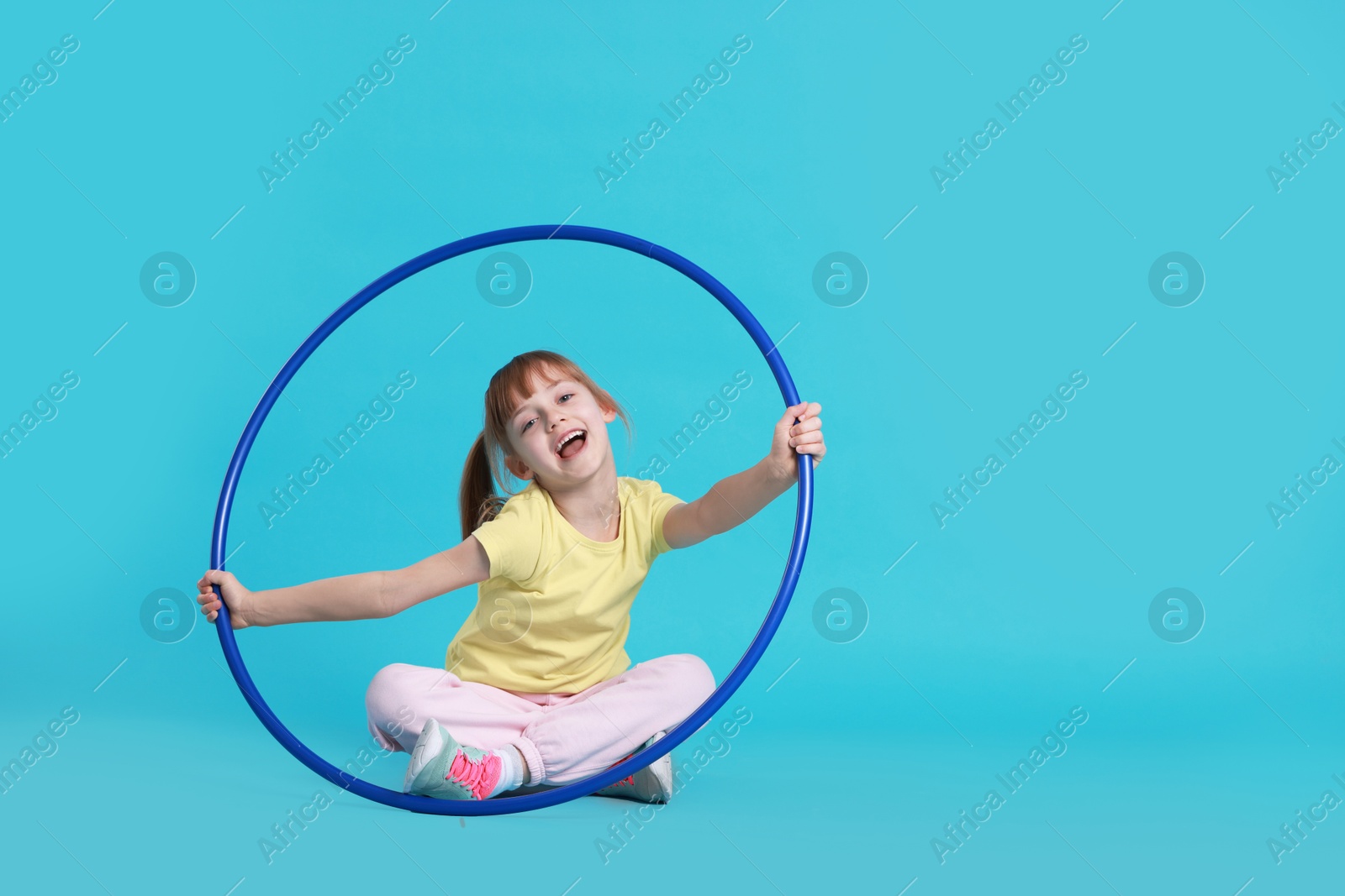 Photo of Cute little girl with hula hoop on light blue background, space for text