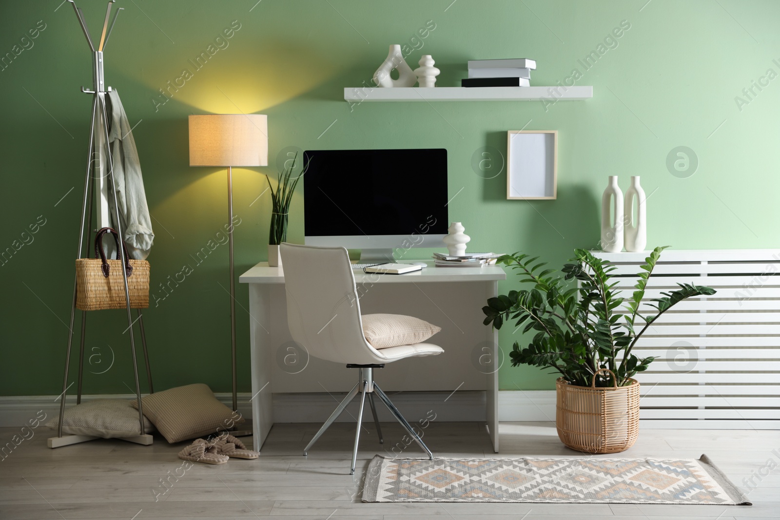 Photo of Home office. Comfortable workplace with desk, computer and lamp near light green wall in room