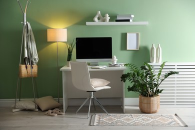 Home office. Comfortable workplace with desk, computer and lamp near light green wall in room