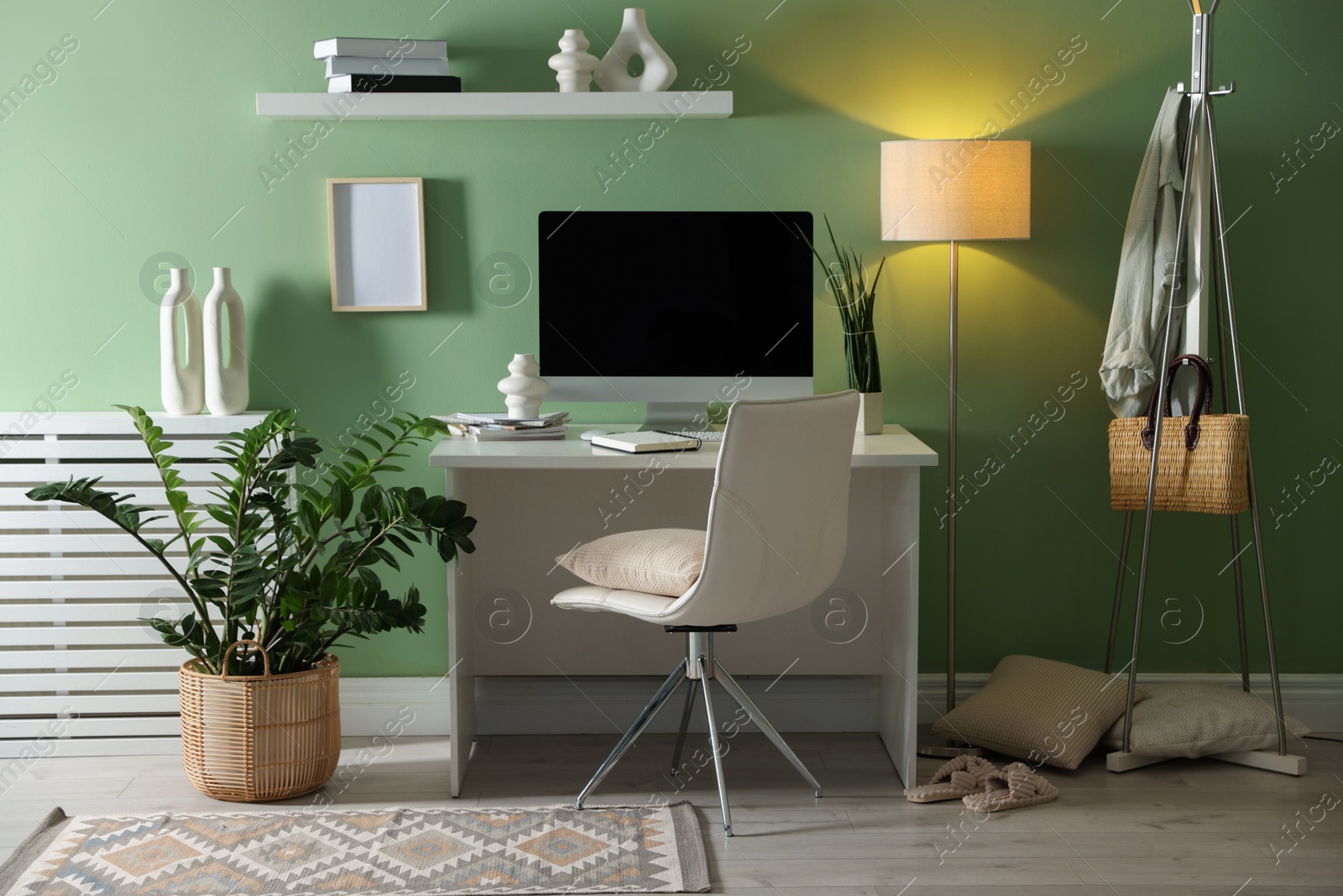 Photo of Home office. Comfortable workplace with desk, computer and lamp near light green wall in room