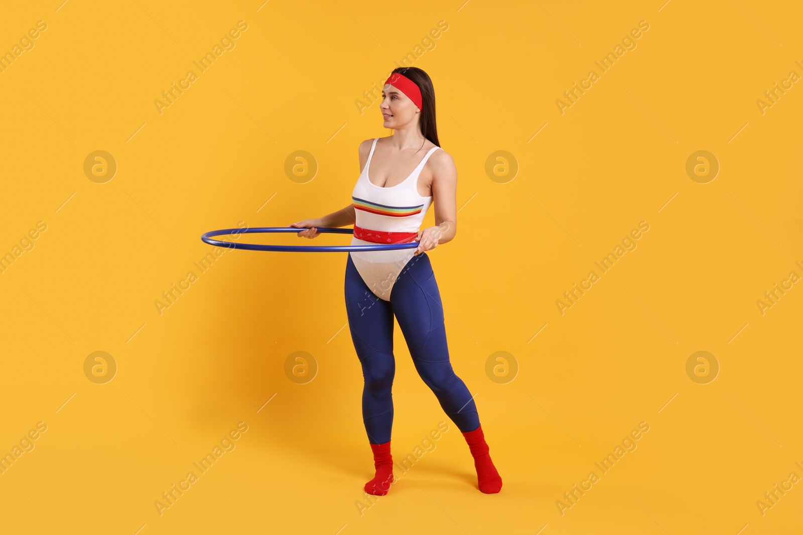 Photo of Smiling woman training with hula hoop on orange background