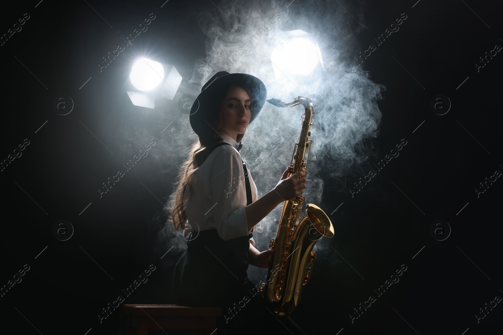 Photo of Professional musician playing saxophone on dark background with lights and smoke