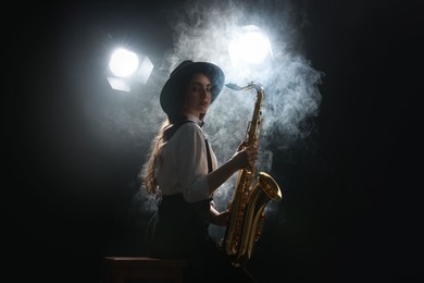 Photo of Professional musician playing saxophone on dark background with lights and smoke