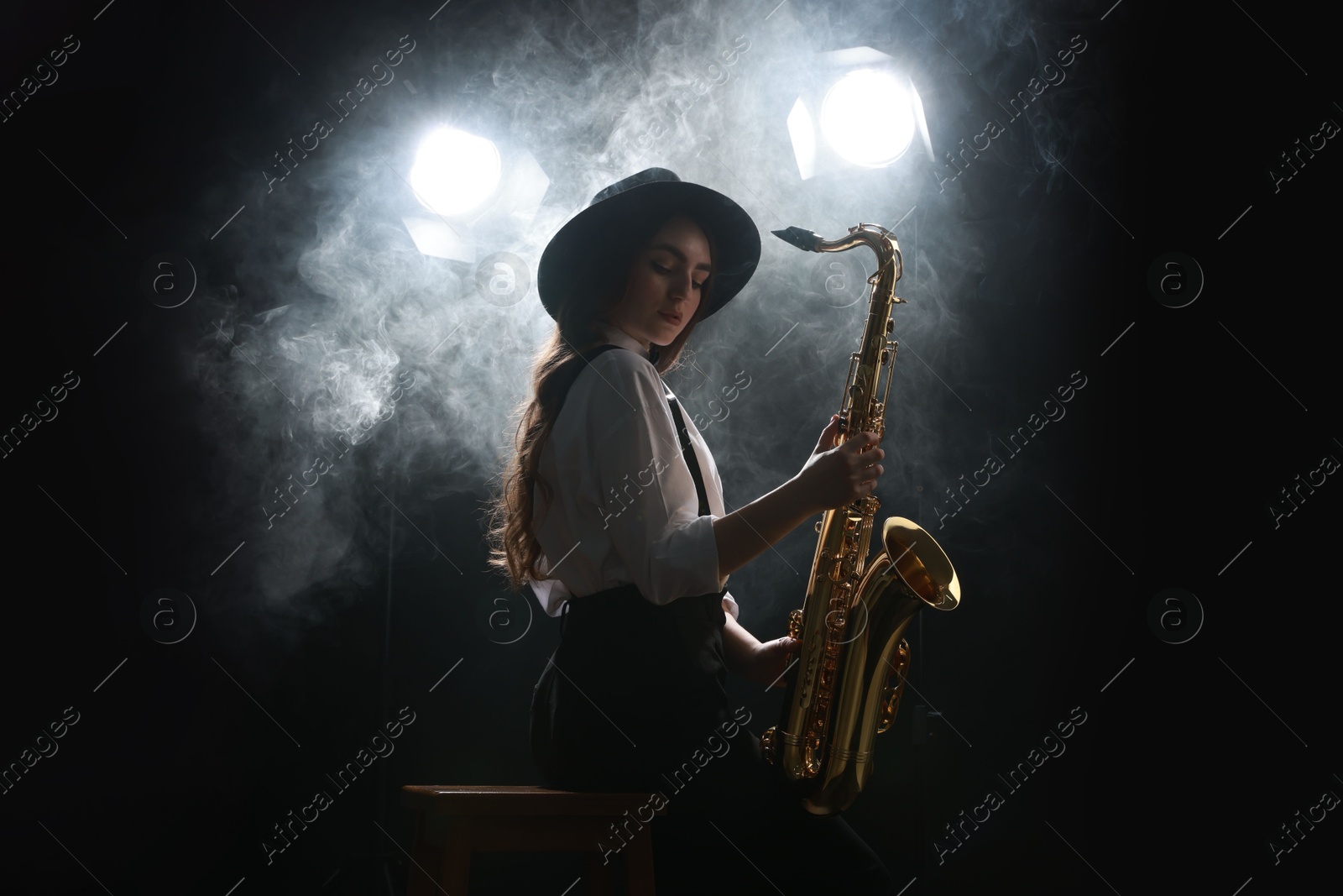 Photo of Professional musician playing saxophone on dark background with lights and smoke