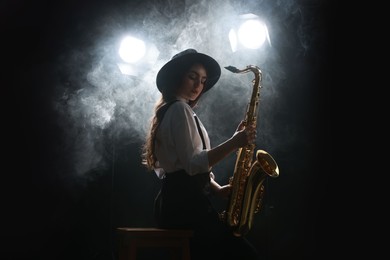 Photo of Professional musician playing saxophone on dark background with lights and smoke