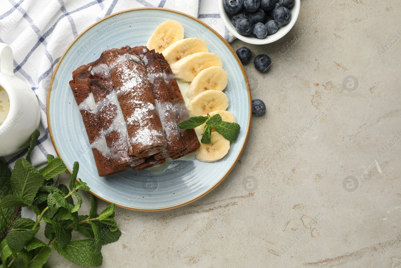 Photo of Delicious chocolate crepes with banana and blueberries served on light table, flat lay