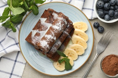 Photo of Delicious chocolate crepes with banana and blueberries served on light table, flat lay