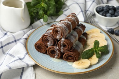 Photo of Delicious chocolate crepes with banana and blueberries served on light table, closeup