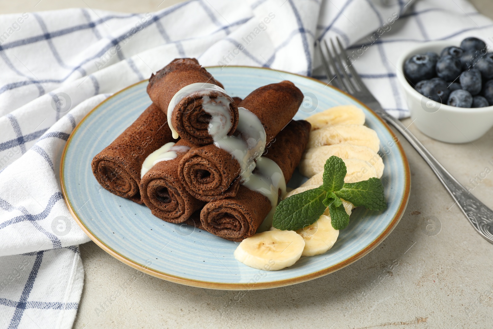 Photo of Delicious chocolate crepes with banana and blueberries served on light table, closeup