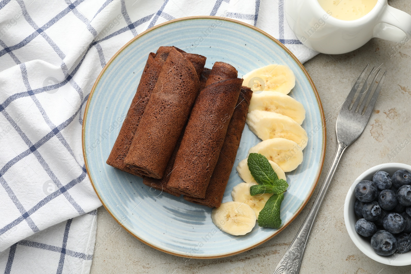 Photo of Delicious chocolate crepes with banana and blueberries served on light table, flat lay