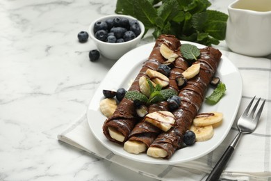 Photo of Delicious chocolate crepes with banana and blueberries served on white marble table, closeup