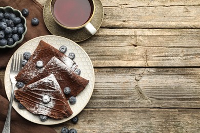 Photo of Delicious chocolate crepes with blueberries served on wooden table, flat lay. Space for text