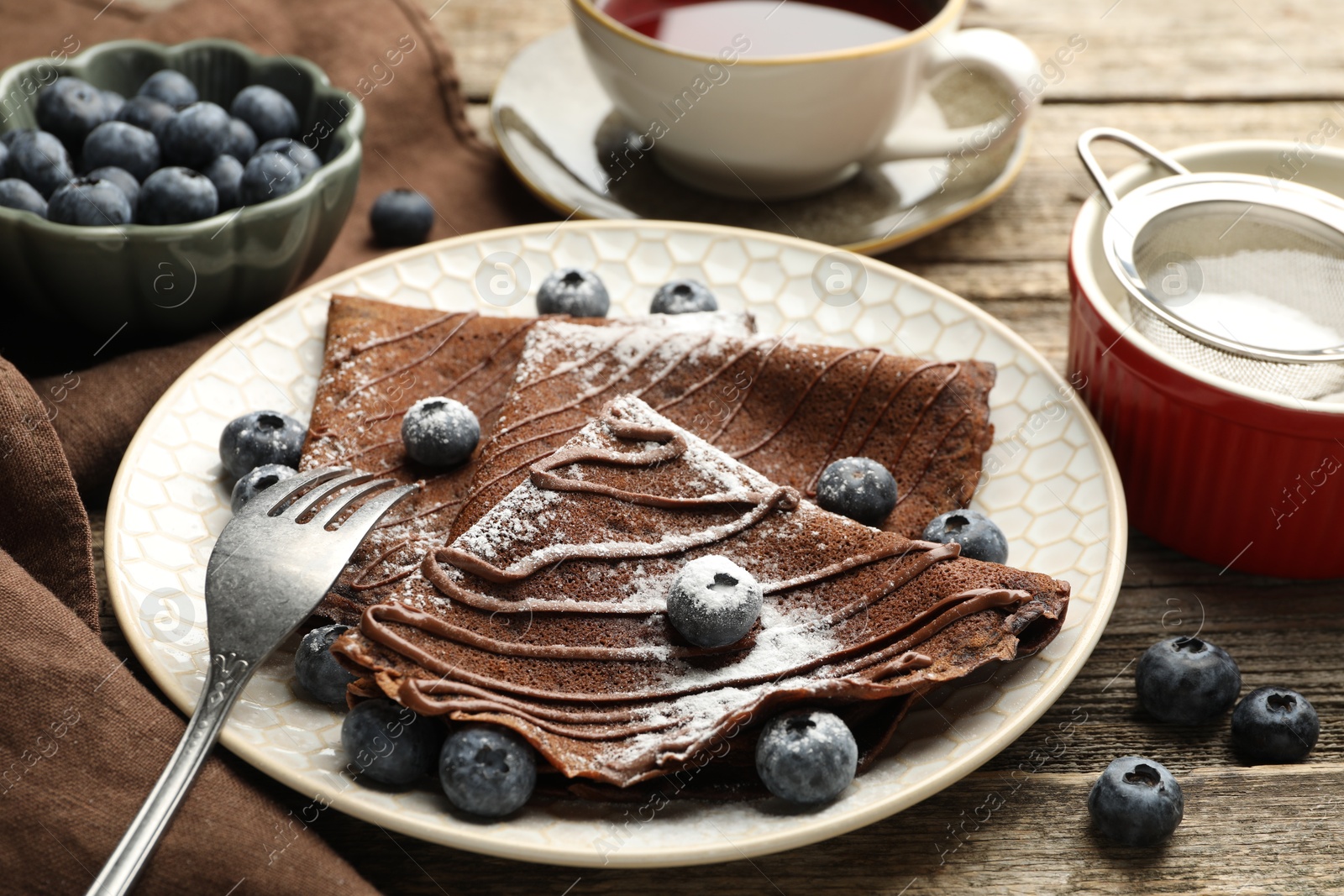 Photo of Delicious chocolate crepes with blueberries served on wooden table, closeup