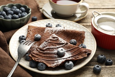 Photo of Delicious chocolate crepes with blueberries served on wooden table, closeup