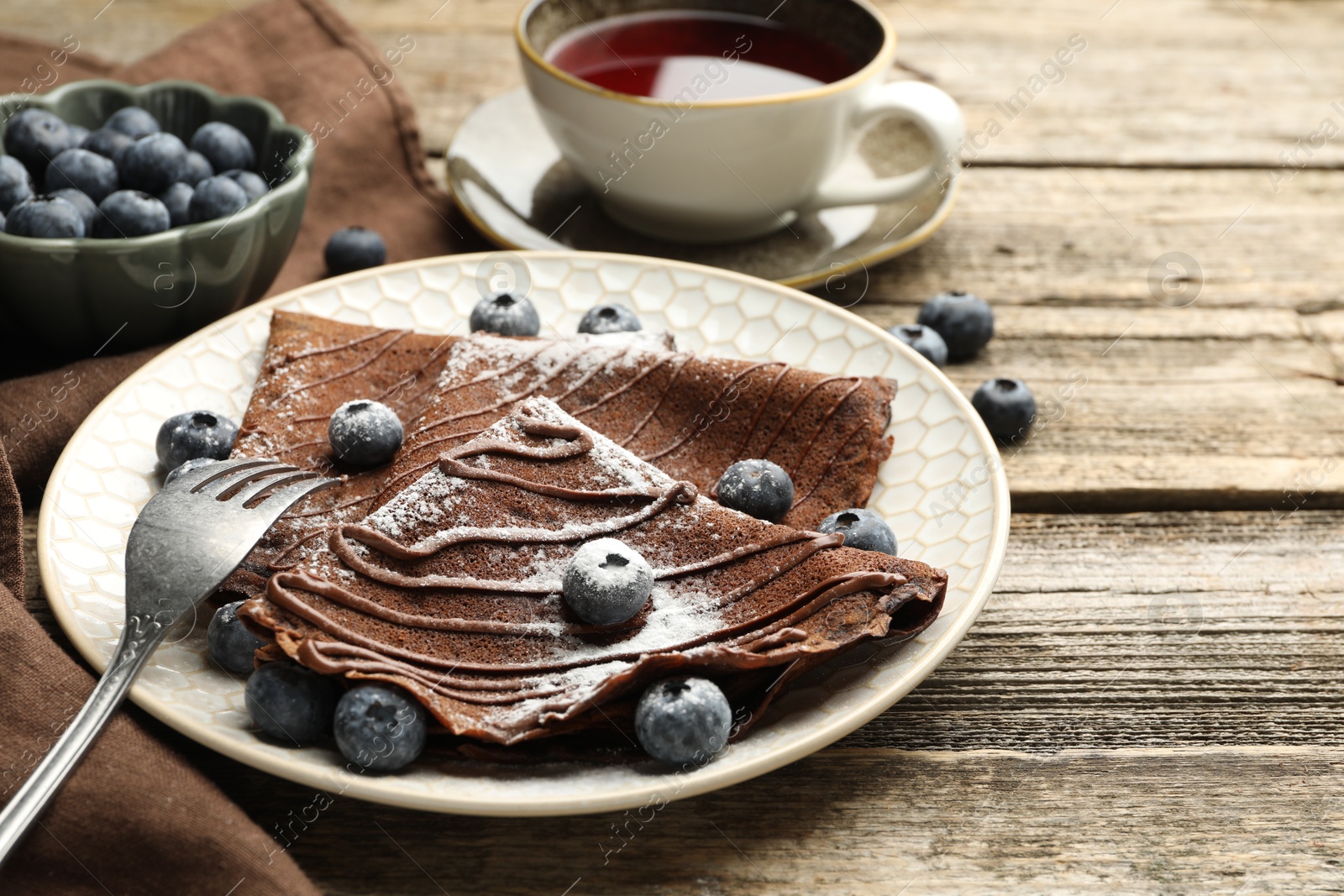 Photo of Delicious chocolate crepes with blueberries served on wooden table, closeup