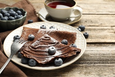 Photo of Delicious chocolate crepes with blueberries served on wooden table, closeup