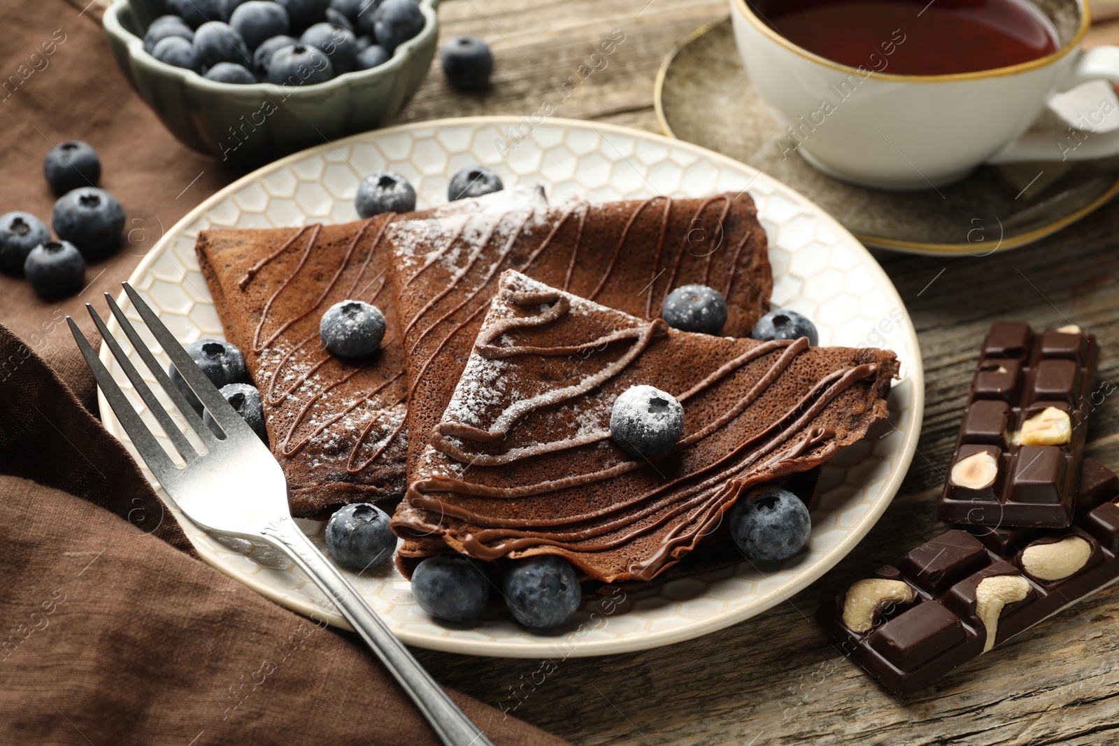 Photo of Delicious chocolate crepes with blueberries served on wooden table, closeup