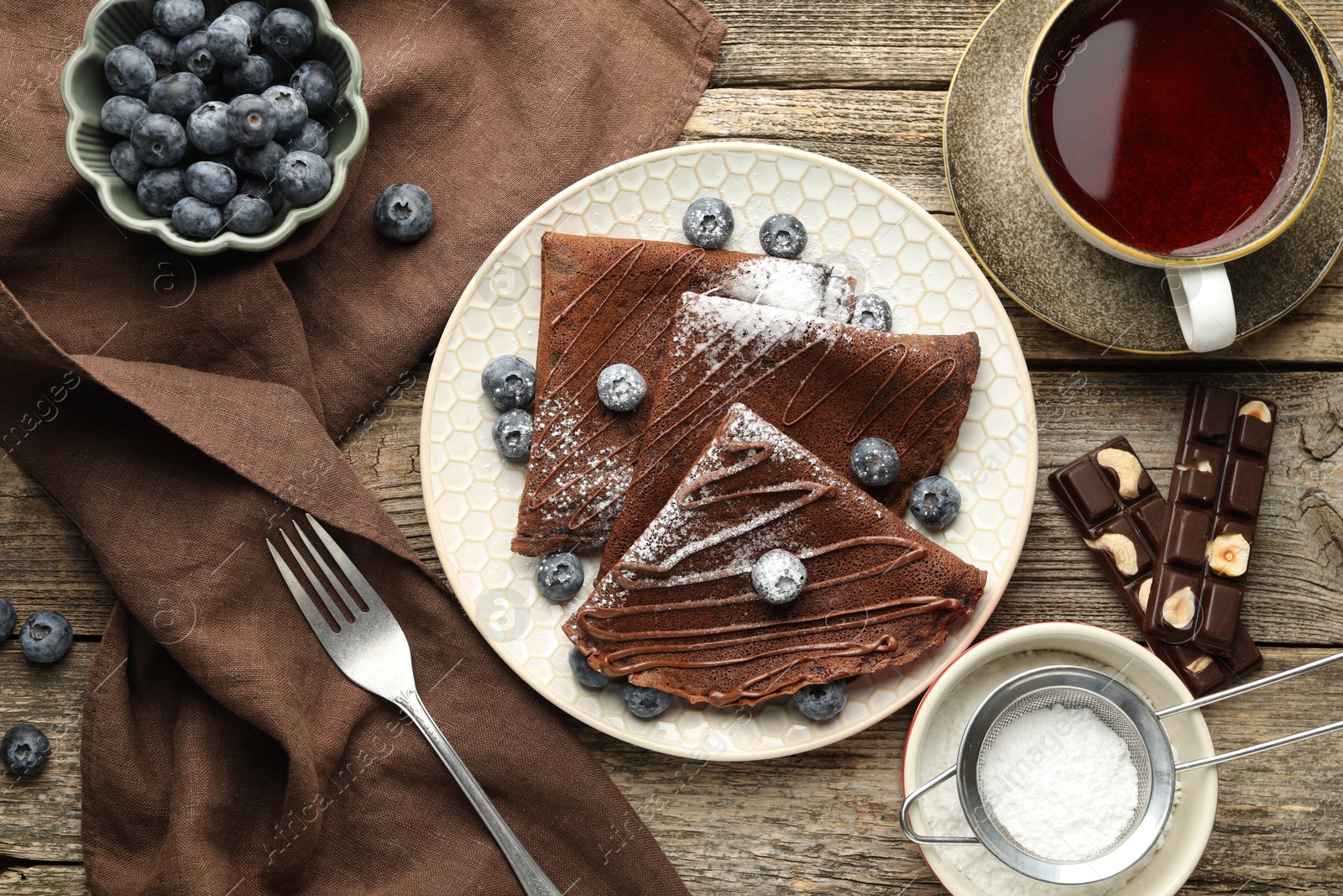 Photo of Delicious chocolate crepes with blueberries served on wooden table, flat lay