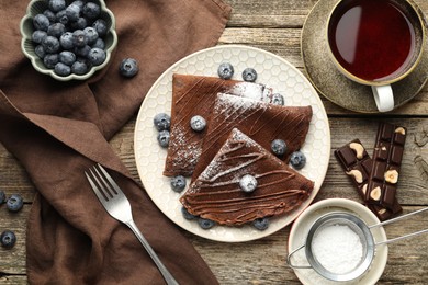 Photo of Delicious chocolate crepes with blueberries served on wooden table, flat lay