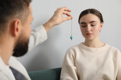 Photo of Psychologist using pendulum while working with patient during hypnosis session indoors