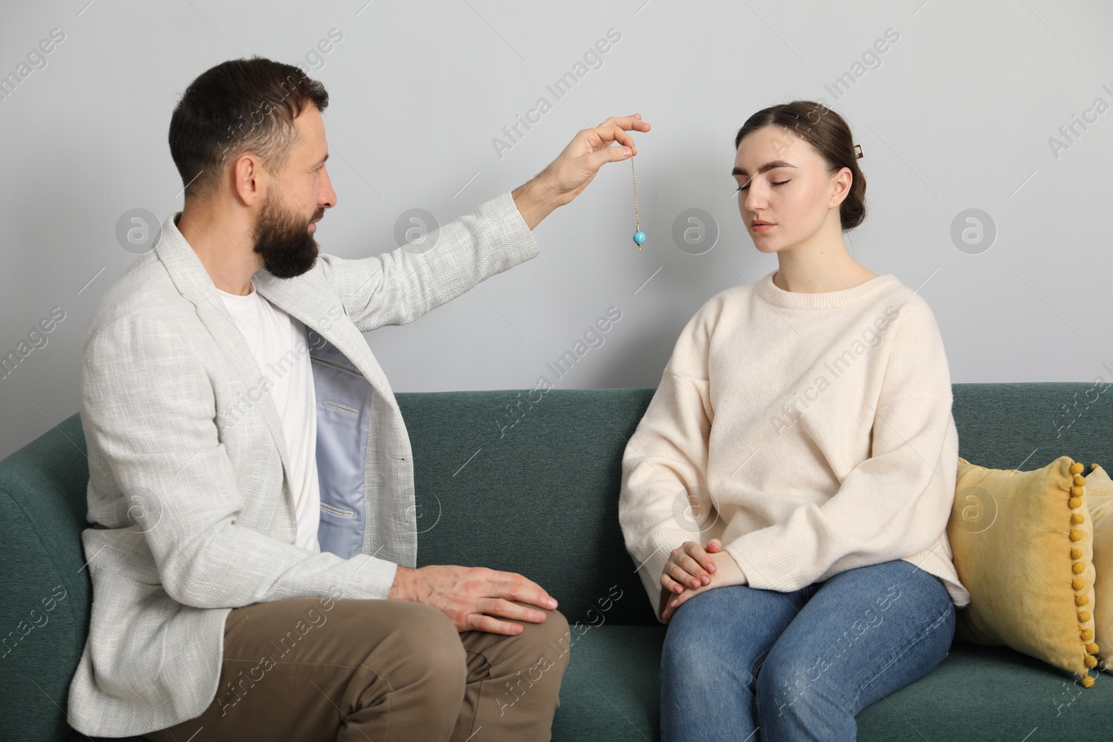 Photo of Psychologist using pendulum while working with patient during hypnosis session indoors