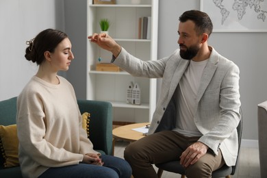 Photo of Psychologist using pendulum while working with patient during hypnosis session indoors