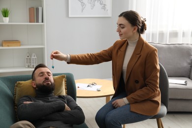 Photo of Psychologist using pendulum while working with patient during hypnosis session indoors