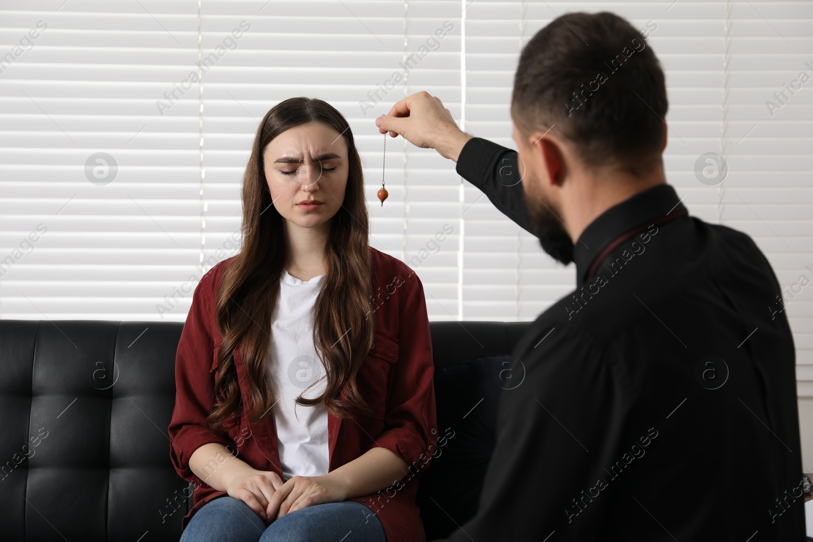 Photo of Psychologist using pendulum while working with patient during hypnosis session indoors