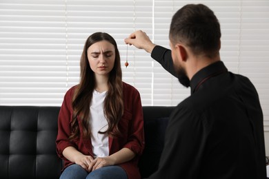 Psychologist using pendulum while working with patient during hypnosis session indoors