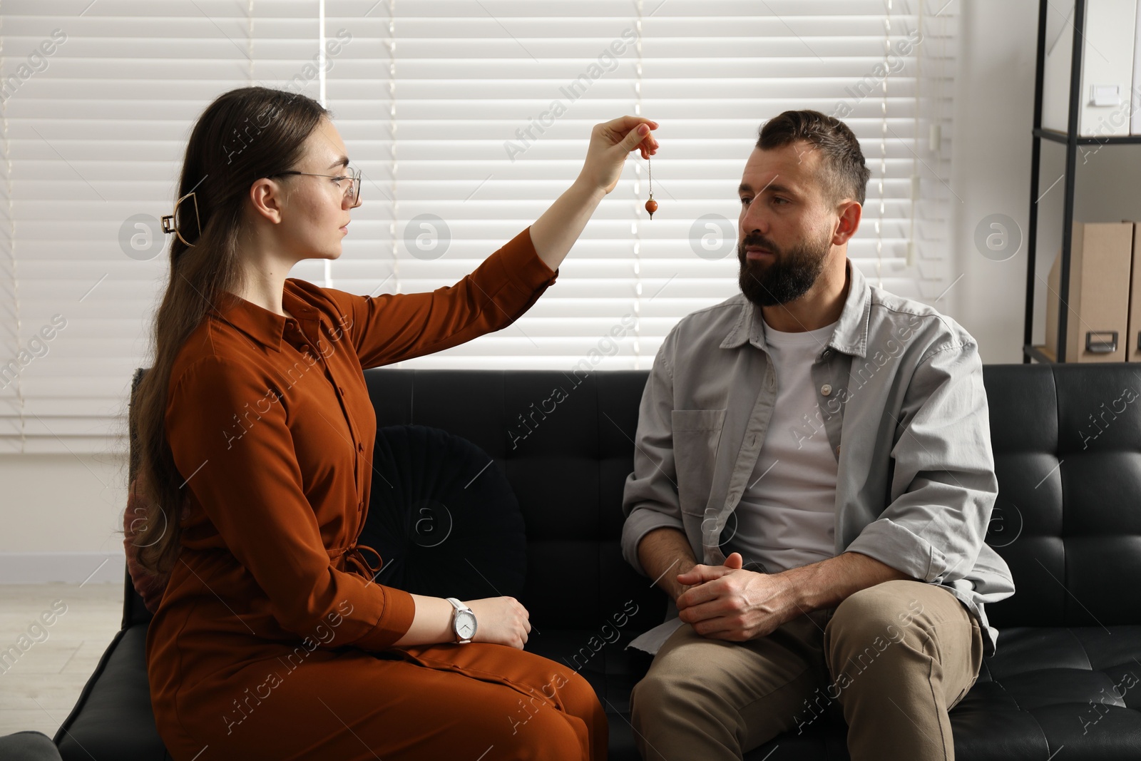 Photo of Psychologist using pendulum while working with patient during hypnosis session indoors