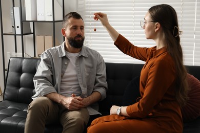 Photo of Psychologist using pendulum while working with patient during hypnosis session indoors