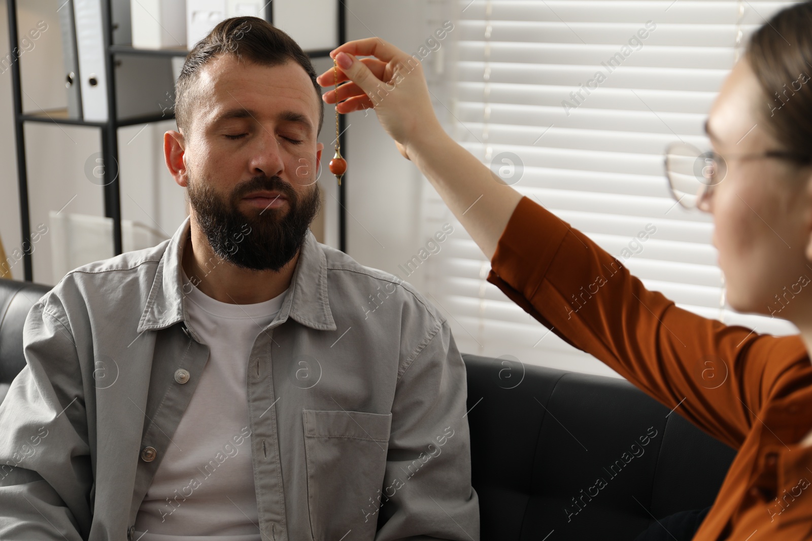 Photo of Psychologist using pendulum while working with patient during hypnosis session indoors, closeup