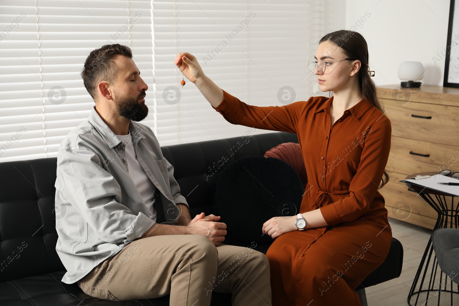 Photo of Psychologist using pendulum while working with patient during hypnosis session indoors