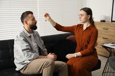 Psychologist using pendulum while working with patient during hypnosis session indoors