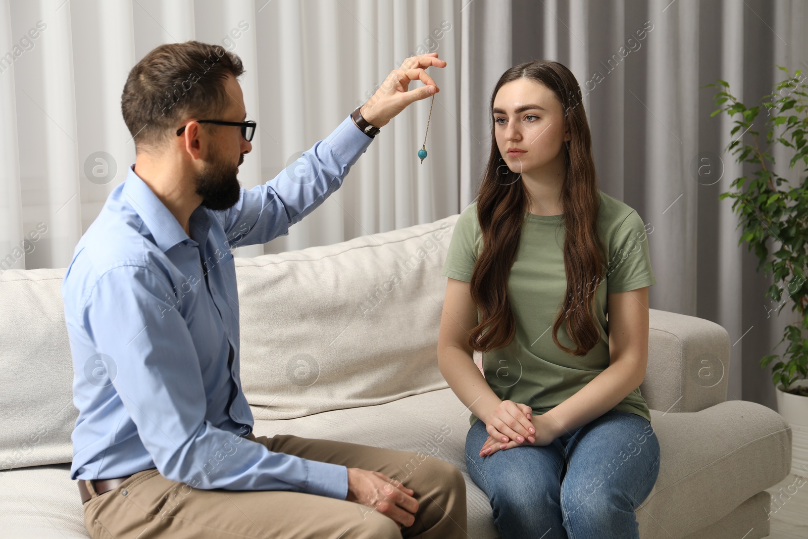 Photo of Psychologist using pendulum while working with patient during hypnosis session indoors