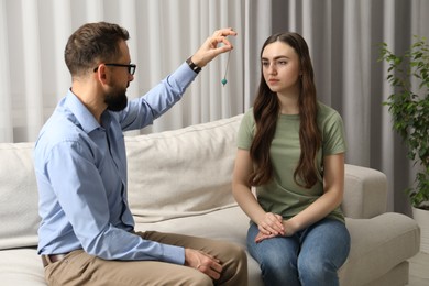 Photo of Psychologist using pendulum while working with patient during hypnosis session indoors