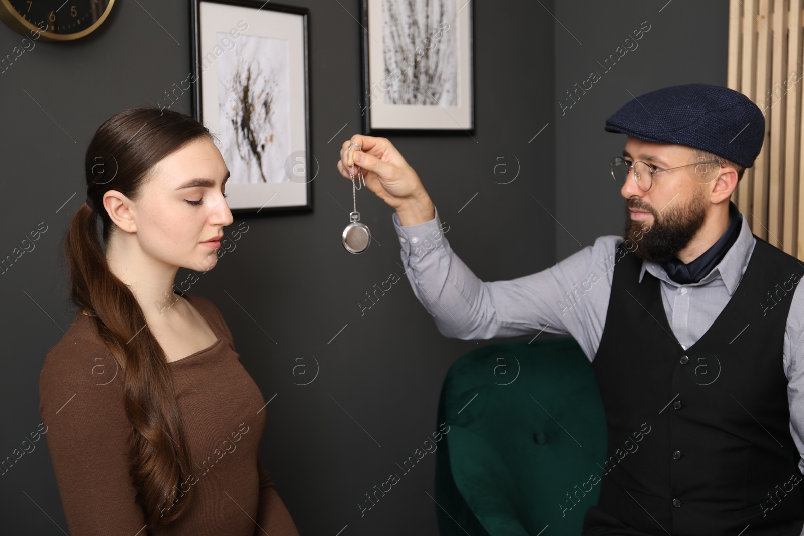 Photo of Psychologist using vintage pocket watch while working with patient during hypnosis session indoors