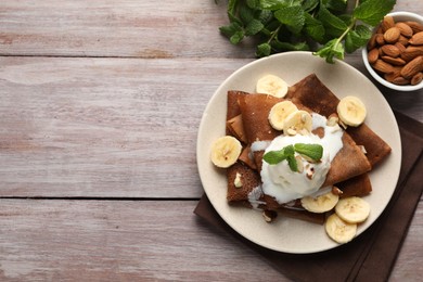 Photo of Delicious chocolate crepes with banana, nuts, mint and scoop of ice cream on wooden table, flat lay. Space for text