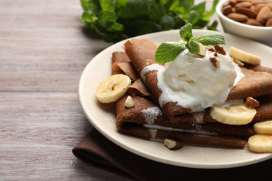 Photo of Delicious chocolate crepes with banana, nuts, mint and scoop of ice cream on wooden table, closeup. Space for text