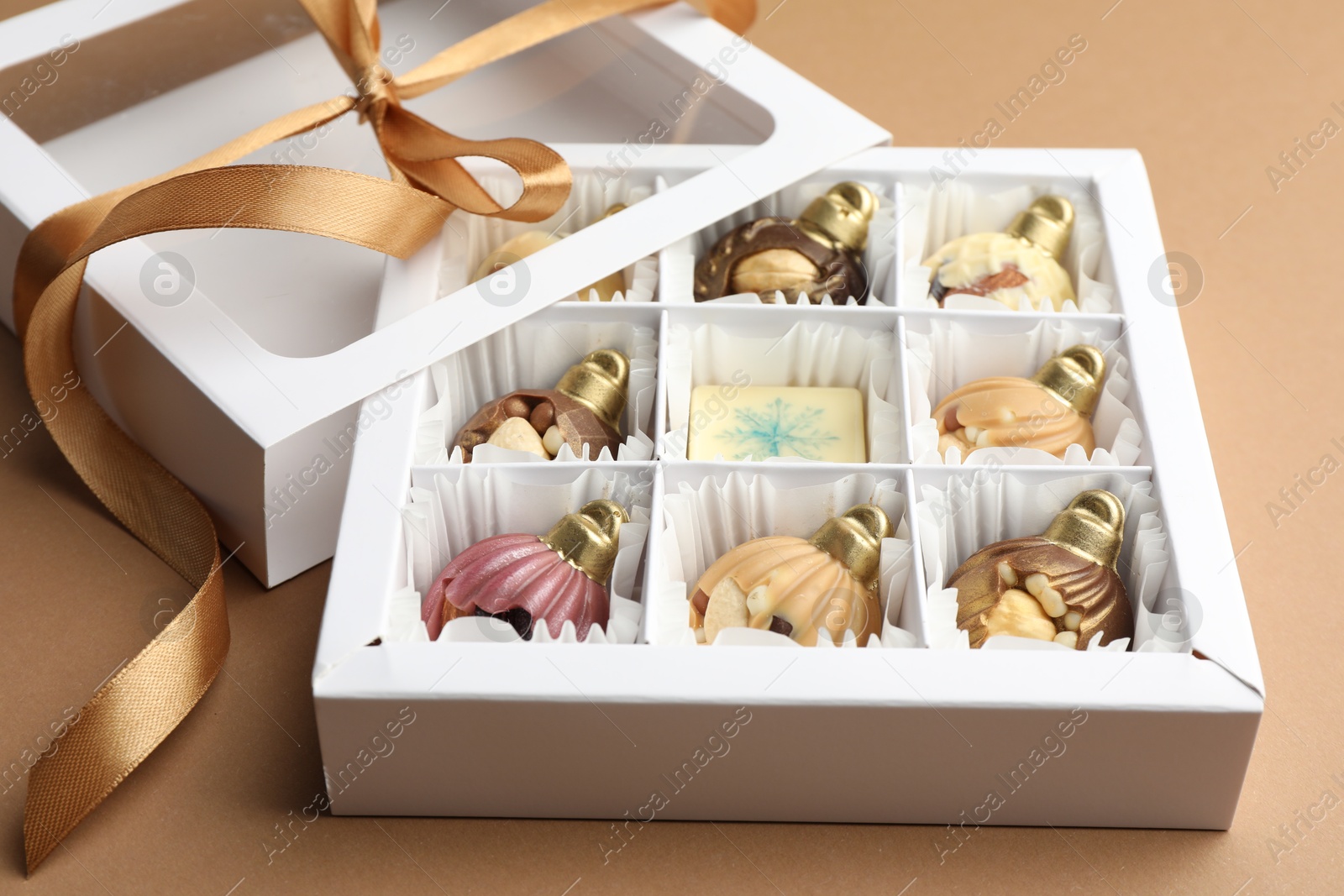 Photo of Delicious chocolate in shape of Christmas ornaments in open box on beige background, closeup