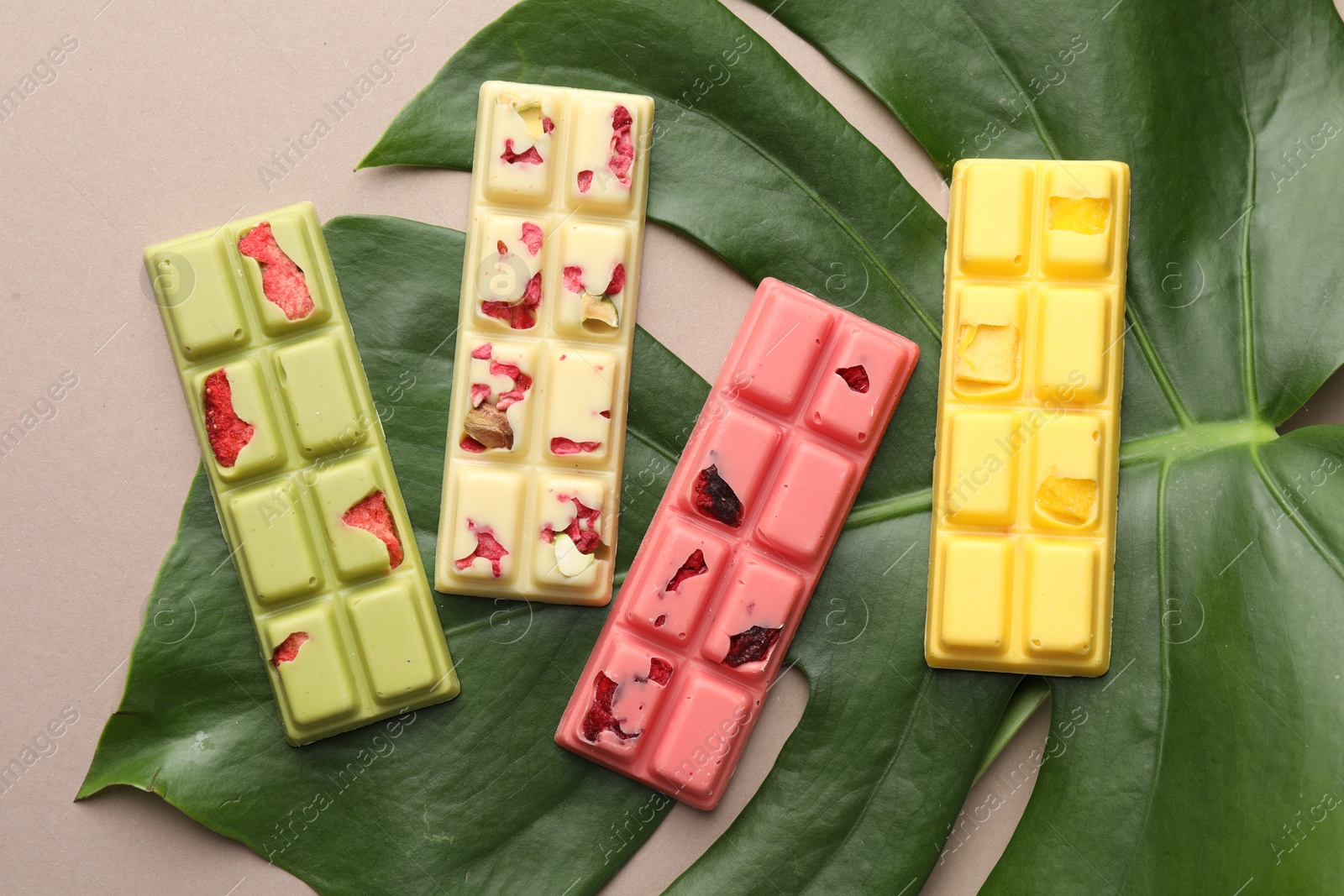 Photo of Different tasty chocolate bars and monstera leaf on beige background, top view