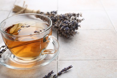 Photo of Aromatic lavender tea in glass cup and dry flowers on white tiled table, closeup. Space for text