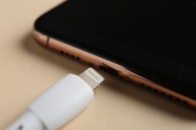 Photo of USB charge cable and smartphone on beige background, closeup